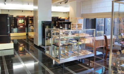 興運堂 宇都宮本店の展示室。ガラスの陳列ケースに仏具が並び、奥の壁沿いにお仏壇が並ぶ。窓から日が入っている